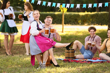 Canvas Print - Young couple in traditional German clothes with beer celebrating Octoberfest outdoors