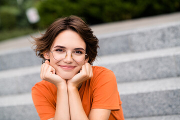 Poster - Photo of dreamy pretty lady wear orange t-shirt spectacles sitting stairs smiling hands arms cheeks outside urban city street