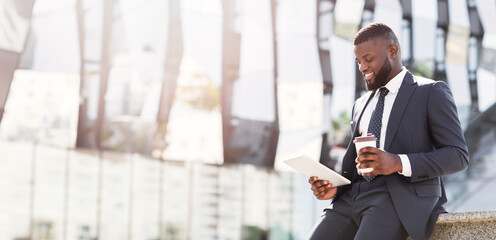 Wall Mural - Positive Black Businessman Using Digital Tablet Computer During Coffee Break Outdoor In City. Free Space