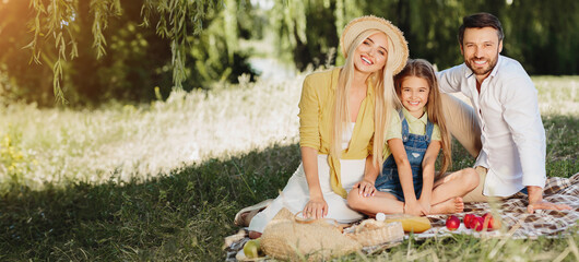 Wall Mural - Family picnic. Parents and daughter resting in nature, smiling to camera, copy space