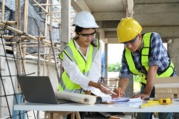 Architects reviewing blueprints and notes on a table at construction site with laptop and architectural model