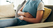 © KayJoint/peopleimages.com - Hands, home and woman with stomach cramps, sick and pain with disease, tummy ache and virus. Closeup, person and girl on couch, illness and tired with digestion, constipation and touching abdomen