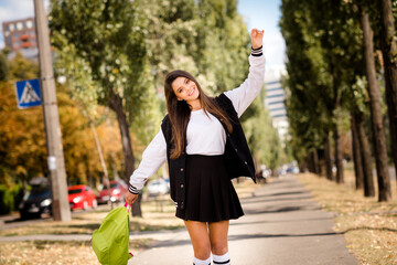 Wall Mural - Photo of optimistic girlish student with straight hairstyle dressed stylish jacket hold bag raising arm up in sunny weather outdoors