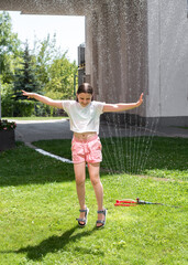 a girl jumps under a sprinkler on a hot summer day