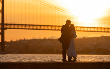 Wall Mural - A couple is kissing in front of a bridge with the sun setting in the background