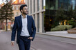 © Liubomir - Confident smiling businessman wearing blazer and glasses walking in urban city street. Professional young man enjoying his day. Concept of success, confidence, business attire.