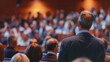 © Pornarun - A large crowd gathers for a conference, listening to a speaker. The audience is engaged and attentive, with many looking towards the stage.