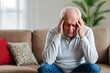 © PNG&Background Image - Senior man sits on a couch at home suffering from a headache or migraine with copy space.