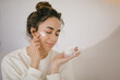 © polinaloves - Young woman 30 years old applying face cream on her skin.