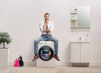 Wall Mural - Pensive businessman sitting on top of a washing machine