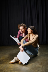 Wall Mural - A good looking man and woman sit closely on the ground during theater rehearsals.