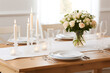 © jamalnasro - Romantic dinner table setting with white candles, flowers and plates on a wooden table.