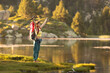 © VICTOR - A woman is standing on a grassy hillside by a lake, holding a pair of poles. She is smiling and she is enjoying the outdoors