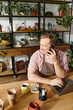 © LIGHTFIELD STUDIOS - A man sitting at a table talking on a cell phone in a plant shop, embodying the concept of owning a small business.