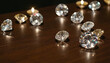© Roman - Several diamonds and two lit candles are arranged on a dark wooden table surface