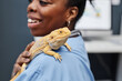 © Seventyfour - Close up of friendly bearded dragon after medical treatment sitting on shoulder of female veterinarian of Black ethnicity holding lizard in tender manner in vet office, copy space