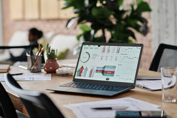 Wall Mural - Wooden work desk with black matt laptop demonstrating analytical research presentation, table full of papers and office supplies