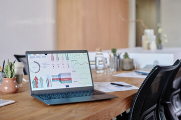 Wall Mural - Medium close up of black laptop demonstrating analytical presentation, wooden table full of office supply and clay pots with green cactuses