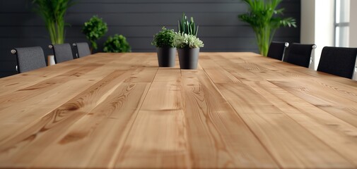 Wide wooden conference table with black chairs and green plants, offering a modern and natural meeting space.