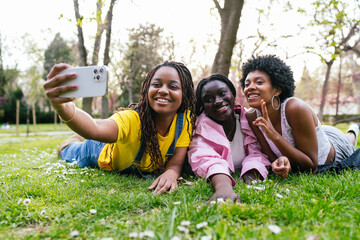 Wall Mural - Three young women are laying on the grass, taking a selfie with a cell phone