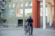 © EDER - smiling african american businessman in suit with backpack walks with electric bike heading to work