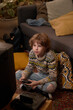 © pressmaster - Vertical shot of male Caucasian teenager sitting cross-legged on carpeted floor with retro controller in hands, looking at old TV and playing video games next to couch in warmly lit living room
