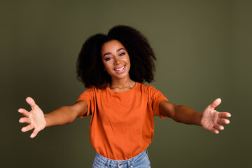 Sticker - Photo of kind positive woman with perming coiffure dressed orange shirt stretching hands to hug you isolated on dark khaki background