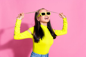 Photo of funky positive girl with dyed hairstyle dressed yellow shirt in sunglass hold her braids isolated on pink color background