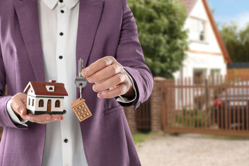 Wall Mural - Real estate agent holding house model and key against future dwelling, closeup