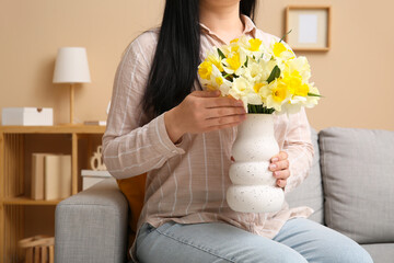 Sticker - Woman holding vase with beautiful narcissus flowers and sitting on sofa in room