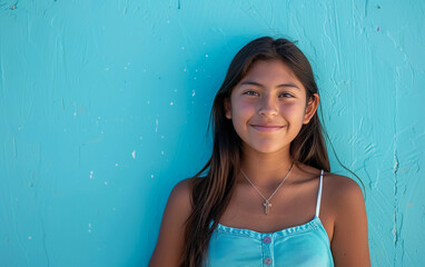 Wall Mural - A young girl is smiling at the camera in a blue tank top. She is wearing a necklace with a cross pendant