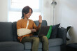 © Queenmoonlite Studio - Injured Asian Man Wearing Medical Support and Arm Sling Bandage Greetings With Waving Hand On Laptop At Home.