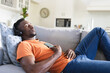 © Wavebreak Media - African american man relaxing on sofa in headphones, listening to music using smartphone