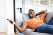 © Wavebreak Media - Happy african american man relaxing on sofa watching tv, using remote control