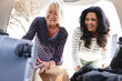 © Wavebreak Media - Two happy diverse senior female friends going on trip packing car boot with luggage
