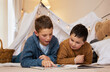 © CineLens2024/peopleimages.com - People, kids and brothers on floor with reading book in bedroom for bonding, education and learning. Family, boys and magazine for child development or growth at home for knowledge or information