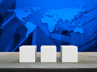 Poster - Three white block cubes on wooden table over world map, modern office city tower and skyscraper, Elements of this image furnished by NASA