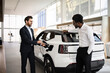 © sofiko14 - Dealer shows electric SUV to businessman in car dealership. Sales process demonstrates environmental consciousness and advances in automotive technology.