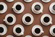 © Sourav Mittal - Photo of white coffee cups with black coffee on saucer, arranged in rows in a neat geometric pattern on a brown background, in a flat lay, top view.