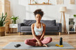 © LIGHTFIELD STUDIOS - Curly African American woman in activewear practicing yoga on a mat in a cozy living room setting.