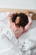 © LIGHTFIELD STUDIOS - Curly African American woman in pajamas peacefully laying on a bed with white sheets in the morning.