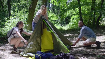 Fototapete - A family sets up a tent together in nature on a sunny summer day. They work as a team, helping each other to prepare their campsite.