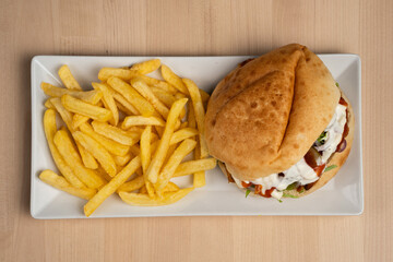 Top view of delicious sandwich with fries served on a white plate over wooden table