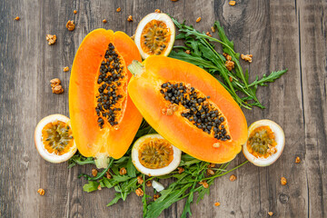 Slices of sweet papaya, passion fruit and rucola surrounded by granola flakes on a wooden background