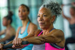 © anzodesign - Senior woman exercising on rowing machine in a group fitness class