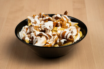 Wall Mural - Bowl of loaded fries topped with creamy sauce and grilled chicken on a wooden table