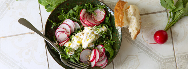 Wall Mural - bowl of salad with arugula, radishes and stracciatella cream cheese on a light table, top view