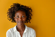 © OPPERMAN - Curly haired woman posing in front of yellow wall.