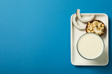 Wall Mural - Glass of alternative milk, coconut and nuts in bowl on blue background, space for text