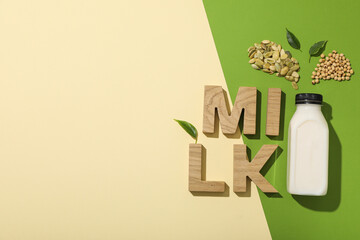 Wall Mural - Bottle of alternative milk and wooden letters on beige and green background, space for text